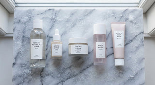 Five minimalist Korean skincare products arranged in a clean line on a frost-dusted marble surface under soft natural light.